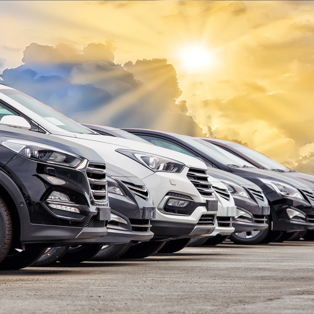 A row of new cars parked in front of a bright sun, showcasing their sleek designs and vibrant colors.